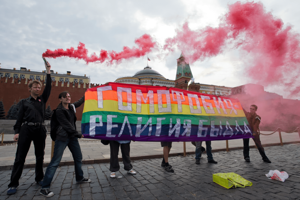 Ativistas LGBTI+ seguram uma faixa onde se lê: "Homofobia - a religião dos agressores", enquanto protestam na Praça Vermelha em Moscovo, Rússia, a julho de 2023